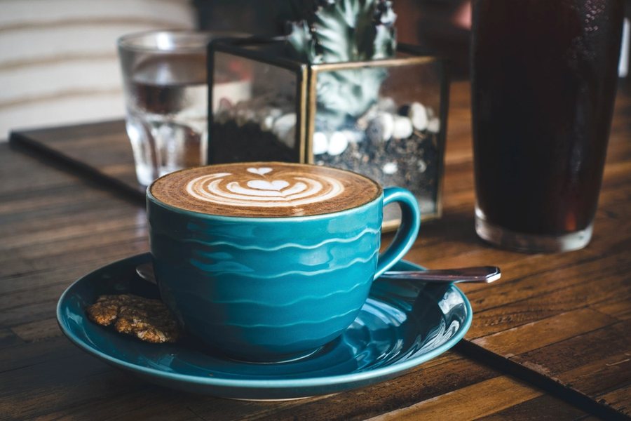 Un cappuccino dans une tasse turquoise, sur une table de bois sombre