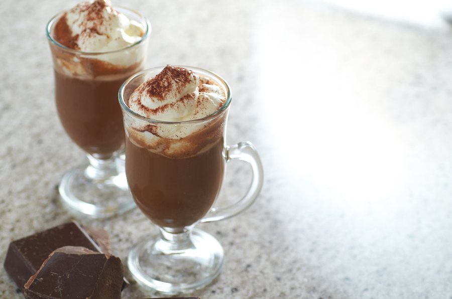Deux verres de chocolat chaud sous la chantilly poudrée de cacao, des carrés de chocolat à côté