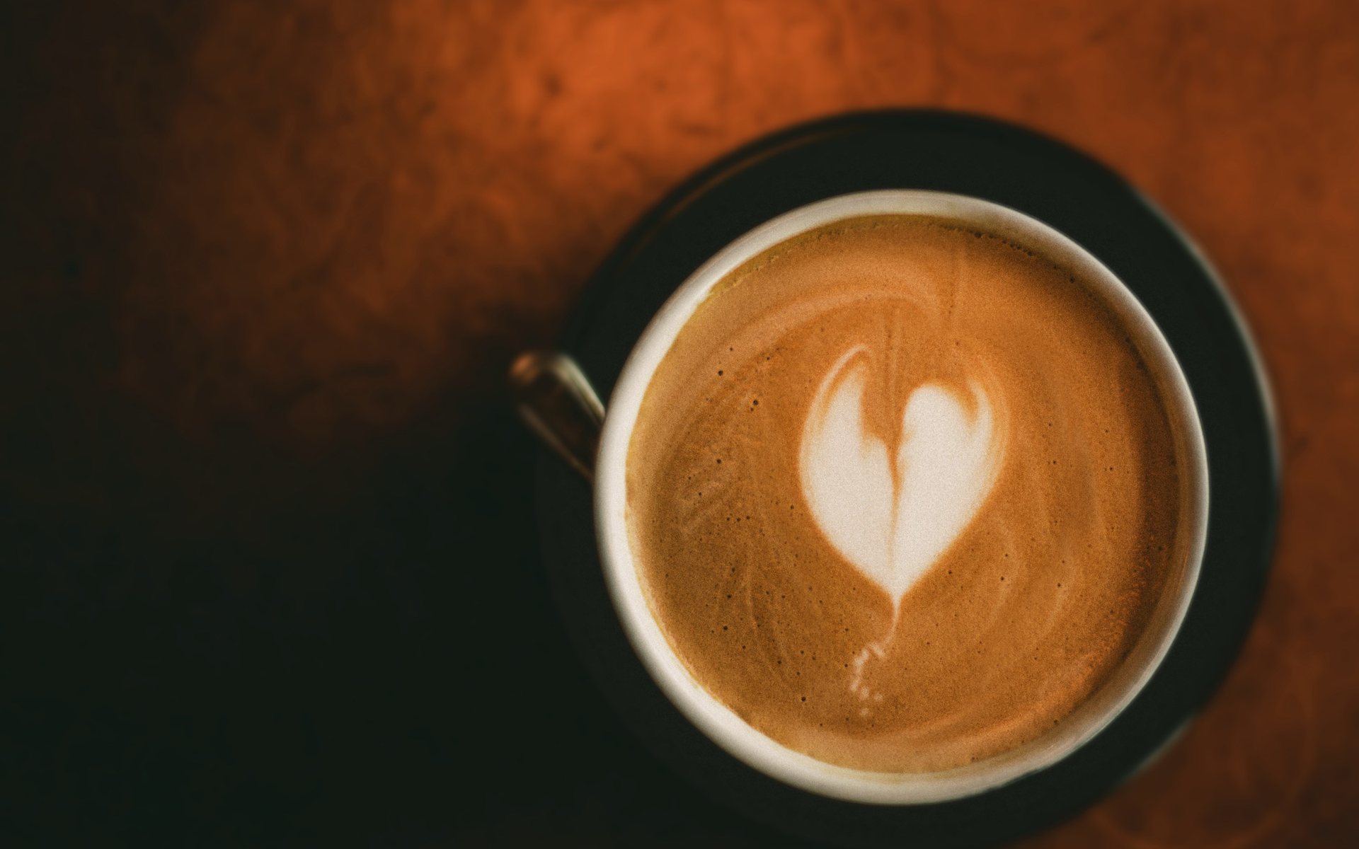 Un café au lait vu d’en haut, un cœur dessiné dans la mousse, sur une table sombre