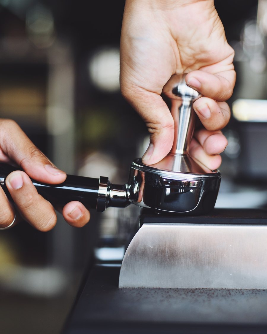 Deux mains tassent le café moulu dans le porte-filtre